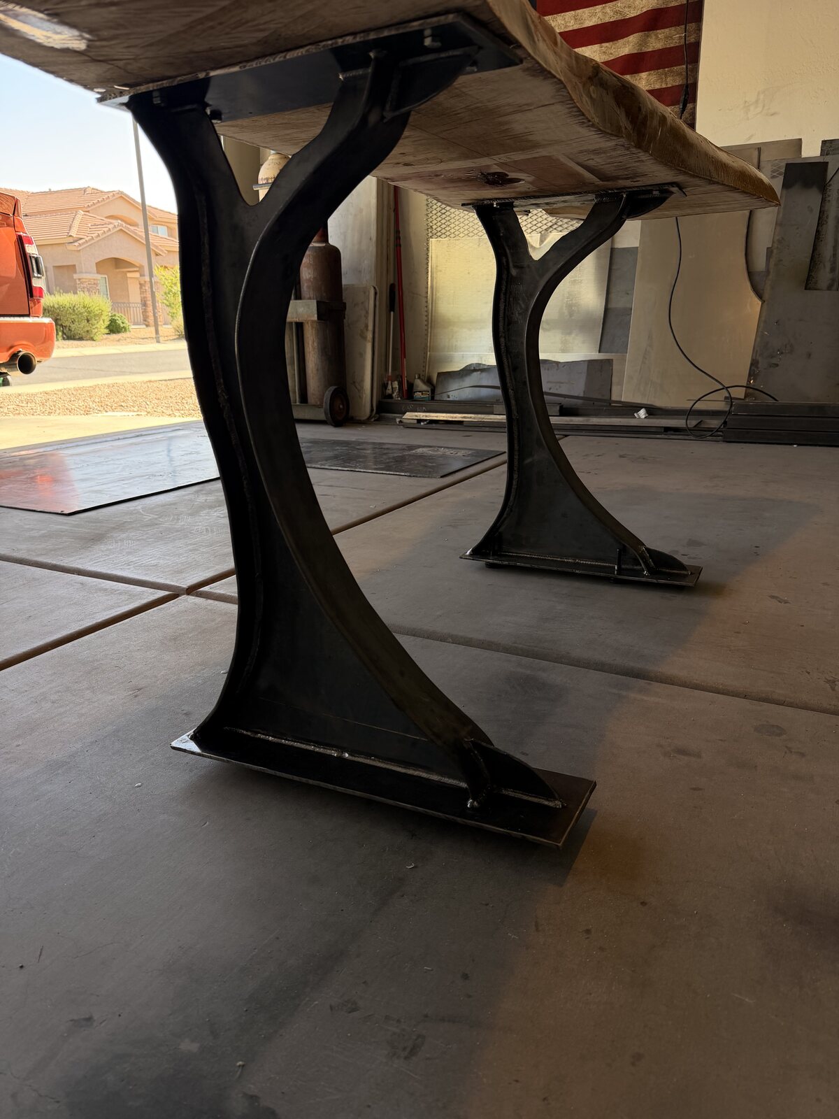 Curved black steel wishbone desk legs welded and bolted under a live-edge slab