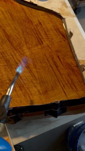 Torch flame passing over a live-edge mesquite slab in the shop